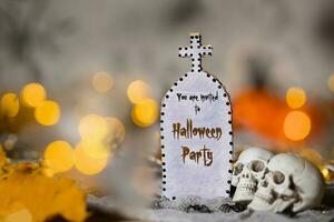 You are invited to Halloween party. Grave and two skulls. Closeup photo