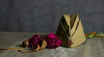 Military cap, carnations, Saint George ribbon on a wooden surface. photo