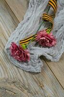 Two pink carnations, Saint George ribbon on a wooden surface. photo