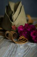 Military cap, carnations, Saint George ribbon on a wooden surface. photo