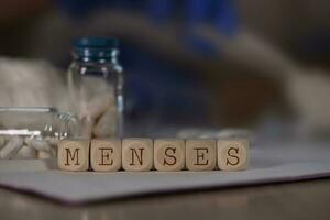 Word MENSES composed of wooden dices. Pills, documents and a pen in the background. photo