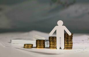 Paper cutout of a person in front of coins stacks. photo