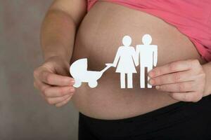 Young pregnant woman keeps paper cutouts of a family. Closeup photo