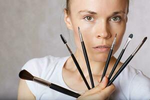 Young lady keeps make up brushes kit close to her face. Closeup photo