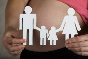 Young pregnant woman keeps paper cutouts of a family. Closeup photo