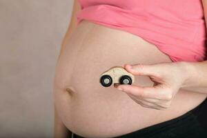 joven embarazada mujer mantiene pequeño de madera vehículo. foto