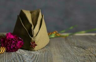 Military cap, carnations, Saint George ribbon on a wooden surface. photo