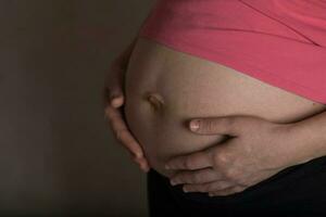 joven embarazada mujer toques su barriga. dramático ligero. foto