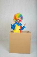 Boy of five years dressed in the costume of a clown stays in a carton paper box. photo