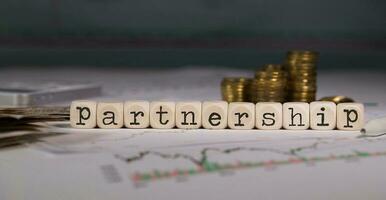 Word PARTNERSHIP composed of wooden letter. Stacks of coins in the background. photo