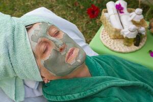 A senior's face is covered by clay facial mask.Close up photo