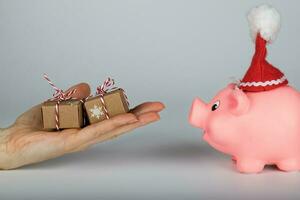 Pink piglet in a Santa Claus hat and human hand with Christmas presents in front of it. photo