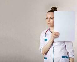 joven hembra médico vestido en un blanco médico uniforme mantiene un sábana de papel. foto