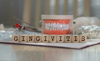 Word GINGIVITIS composed of wooden dices. Pills, documents, pen, human jaw model in the background. photo