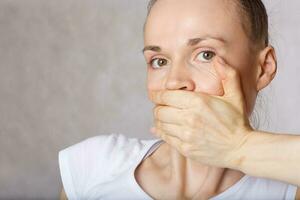 Mouth of young caucasian lady closed by another hand. Closeup photo