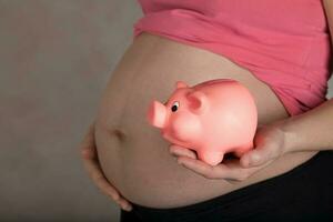 joven embarazada mujer mantiene rosado cerdito banco. foto