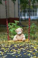 Brown plush teddy bear on a yellow colourful swing. photo