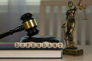 Word DEFENDANT composed of wooden dices. Wooden gavel and statue of Themis in the background. photo