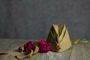 militar gorra, claveles, Santo Jorge cinta en un de madera superficie. foto