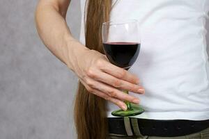 Young lady dressed in jeans keeps a glass of red wine. Closeup photo