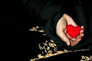 Palm of a peasant woman with plush red heart on a black fabric. photo