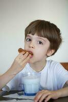 chico de seis años es tomando un vaso de calentar Leche con avena galletas. foto