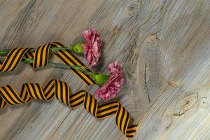 Two pink carnations, Saint George ribbon on a wooden surface. photo