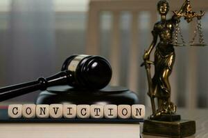 Word CONVICTION composed of wooden dices. Wooden gavel and statue of Themis in the background. photo