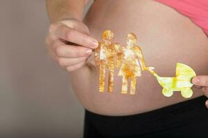 Young pregnant woman keeps paper cutouts of a family. Closeup photo