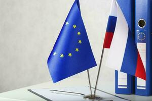 Two flags of the EU and Russia on a white table. Closeup photo