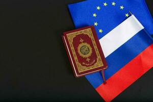 Flags of EU and Russia and the Koran on a black surface. photo