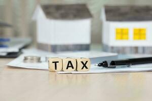 Word TAX composed of wooden letters in front of handmade house. photo