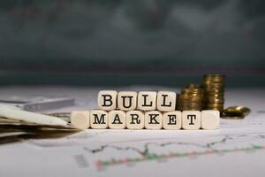 Word  BULL MARKET composed of wooden letter. Stacks of coins in the background. photo