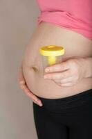 joven embarazada mujer mantiene vacío orina envase cerca a su barriga. foto