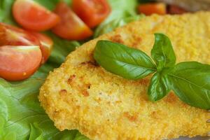 Chicken schnitzel with cherry tomatoes and green salad leaves. photo