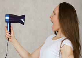 Young lady tries to dry her hair with hairdryer photo