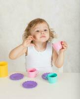 Small girl plays with toy kitchen utensils and dishes. Closeup photo