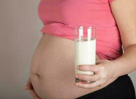 joven embarazada mujer mantiene un vaso de leche. foto