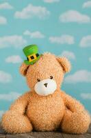 Brown plush teddy bear in a leprechaun hat on a wooden surface. photo