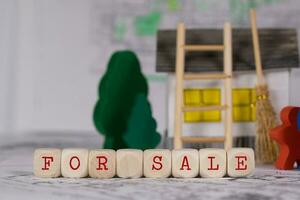 Words FOR SALE composed of wooden letter. Small paper house, wooden trees in the background. photo