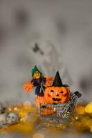 Witch and orange pumpkin in black hat in the small shopping cart. Closeup photo