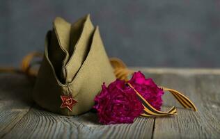 Military cap, carnations, Saint George ribbon on a wooden surface. photo