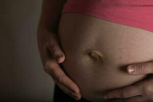 Young pregnant woman touches her belly. Dramatic light. photo