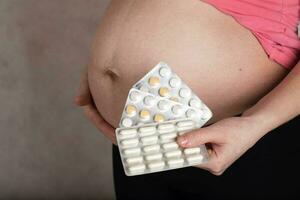 Young pregnant woman keeps films of pills close to her belly. photo