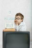 Boy of seven years old looks at white cage which is laced on old TV. photo