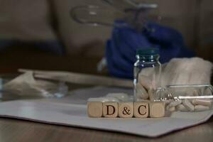 Abbreviation D C for dilation and curettage composed of wooden dices. Pills, documents and a pen in the background. photo