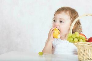 pequeño niña es comiendo Fresco frutas desde un mesa. de cerca foto