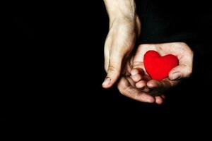 Palm of a peasant woman with plush red heart on a black fabric. photo