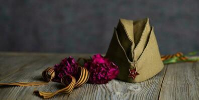 Military cap, carnations, Saint George ribbon on a wooden surface. photo