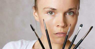 Young lady keeps make up brushes kit close to her face. Closeup photo